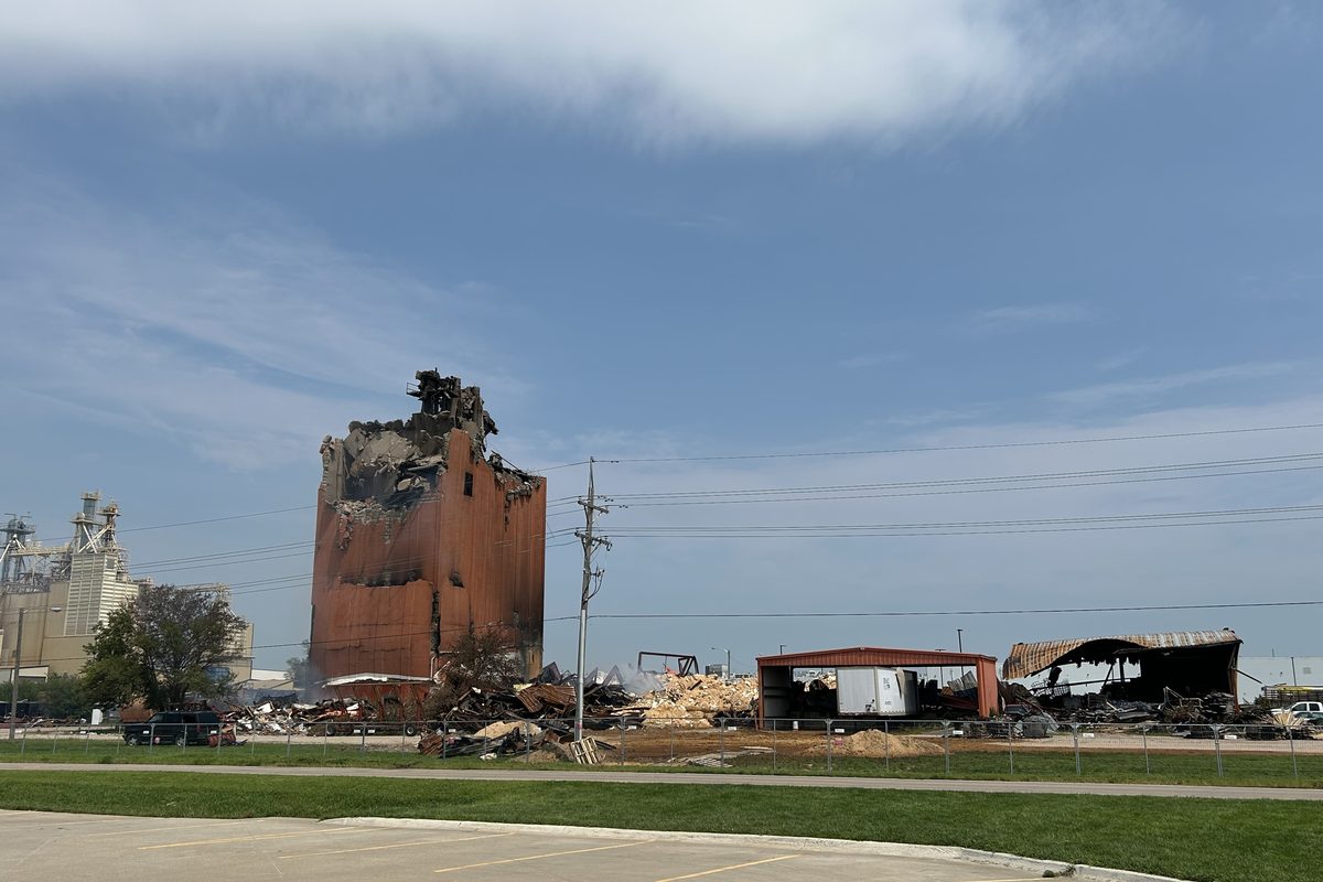 A burnt and partly demolished storage silo standing over the wreckage of the buildings around it.